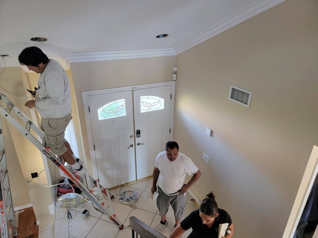 JRS crew at work in a two-story entryway — ladder work at the ceiling line and wall prep below